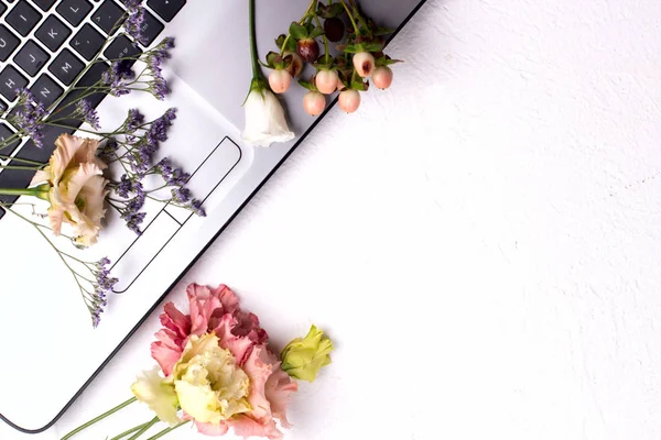 Laptop with flowers and cosmetics on white table. Freelancer workspace.