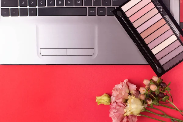 Laptop with flowers and cosmetics on table. Freelancer workspace.