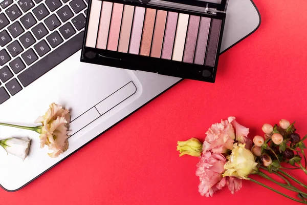 Laptop with flowers and cosmetics on table. Freelancer workspace.