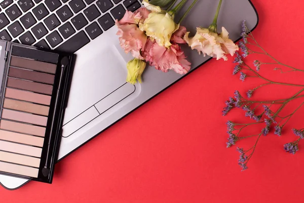 Laptop with flowers and cosmetics on table. Freelancer workspace.