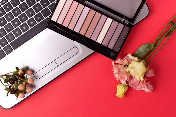 Laptop with flowers and cosmetics on table. Freelancer workspace.