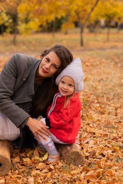 Mutlu anne ve kız sonbahar parkında bir kütükte birlikte poz veriyorlar. Sonbahar havası, sonbahar konsepti, sonbahar