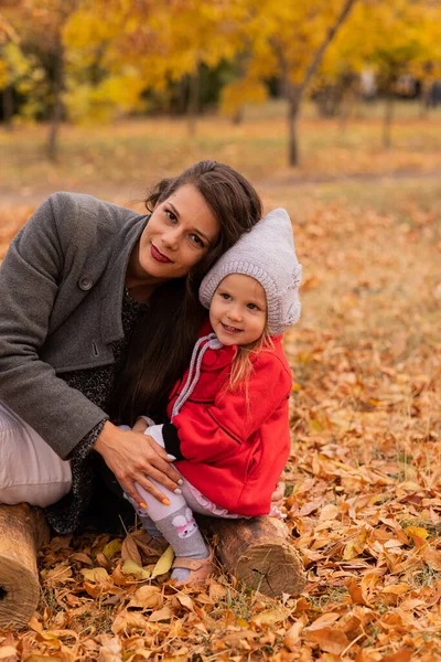 Mutlu anne ve kız sonbahar parkında bir kütükte birlikte poz veriyorlar. Sonbahar havası, sonbahar konsepti, sonbahar