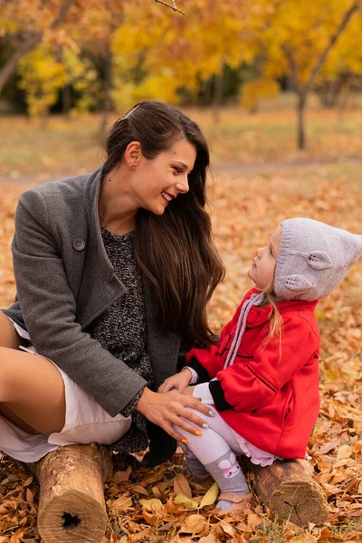 Mutlu anne ve kız sonbahar parkında bir kütükte birlikte poz veriyorlar. Sonbahar havası, sonbahar konsepti, sonbahar