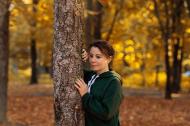 Parkta ağaçta dinlenen gülümseyen bir kadın. Sonbahar mevsimi, sonbahar konsepti, sonbahar