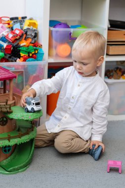 little boy playing with a toy cement truck on a children's treehouse toy in a room with shelves full of toys. childhood, play, and development