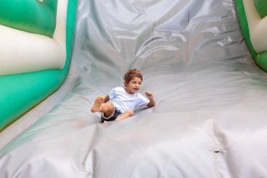 A young boy is having fun sliding down an inflatable bounce house slide