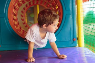 A boy crawls through a colorful tunnel, playing at an indoor playground