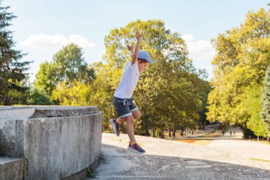 A little boy in a cap jumps high from the stairs in the park