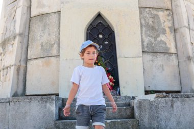 A cheerful boy in a white t-shirt and shorts poses outdoors