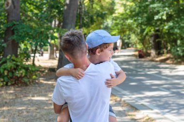 An older brother carries his younger brother in a park on a sunny day