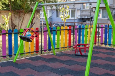 A colorful and inviting children's playground with swings, an empty play area, and a vibrant rainbow-colored fence on a sunny day