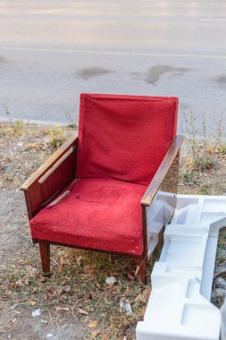 Ahşap kollukları olan yıpranmış kırmızı bir koltuk sokak kenarına atılmış, şehir yoksulluğunu ve çürümeyi sembolize ediyor.