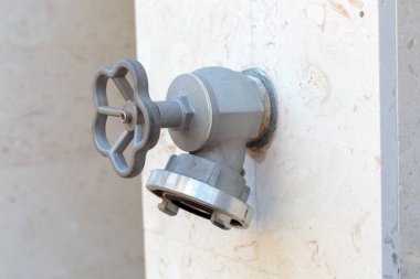 Gri metal bir yangın musluğunun ya da bej renkli mermer bir duvardaki su borusu bağlantısının yakın çekim görüntüsü.