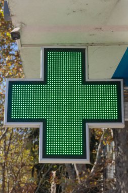 Arka planda bulanık bir sonbahar ağacıyla parlayan yeşil bir eczane işaretinin yakın plan görüntüsü.