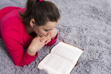 Esmer beyaz kız evde yatakta yatarken kitap okur.
