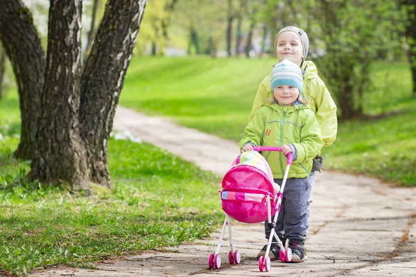 Anak-anak kecil bermain di halaman dengan boneka mainan anak-anak. anak laki-laki dan perempuan bermain game anak-anak bermain kereta bayi di halaman rumah. Persahabatan anak-anak. Anak dengan mainan kereta bayi . — Stok Foto