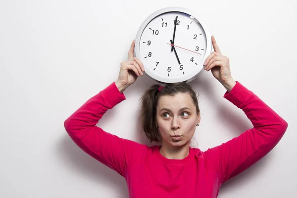 girl is holding watch over her head. concept of time. Time and woman on white wall background. clock in the hands of brunette.