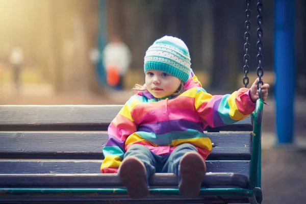 Gadis kecil duduk di ayunan di taman malam. anak adalah naik ayunan kayu pada malam gelap di bawah cahaya dari lentera . — Stok Foto