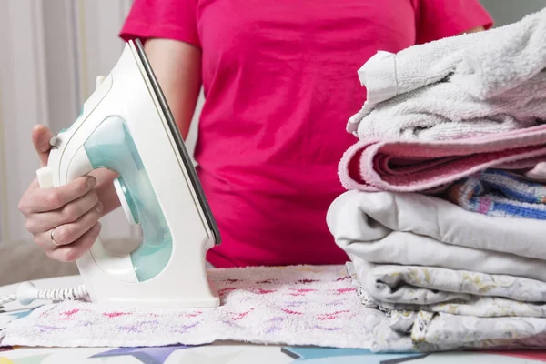 Домохозяйка с утюгом и неглаженым бельем на гладильной доске крупным планом. Женщина гладит одежду в доме . — стоковое фото
