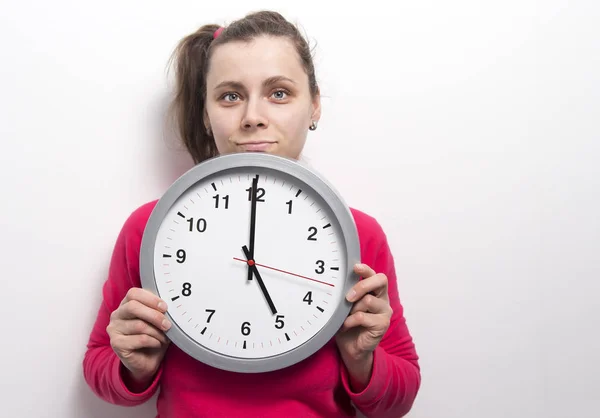 Giovane ragazza bruna caucasica con un sorriso sul suo viso tiene orologio rotondo contro sfondo muro bianco. Il tempo femminile sta andando via concetto. Tempo e donna — Foto Stock