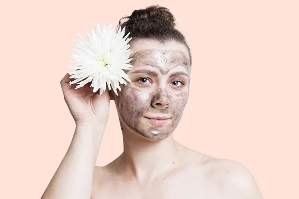 Konsep Skincare. Gadis dengan topeng hitam kosmetik wajah dan dengan bunga putih — Stok Foto