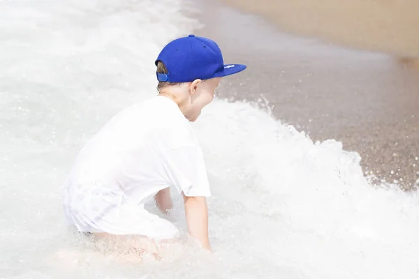 Niño pequeño juega con pequeñas olas en la playa del mar. Niño en vacaciones tropicales de verano bañándose en agua de mar tibia. Feliz chico caucásico en la playa en un día soleado . — Foto de Stock