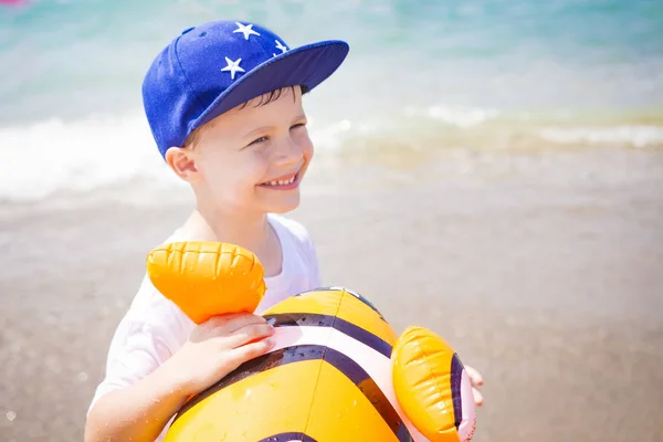 Retrato de niño feliz sonriente en sombrero con globo de pescado de juguete sobre fondo azul de playa de mar. Feliz chico en el mar. Niño en vacaciones tropicales — Foto de Stock