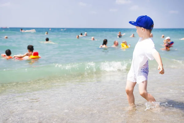 El niño juega en la playa. La gente nada y se relaja en el agua tibia del mar. Playa soleada de verano en vacaciones tropicales. Niño feliz en la playa en un día claro . — Foto de Stock