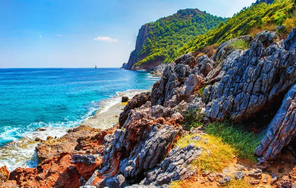 Καταπληκτική θέα σε βραχώδη τροπική παραλία, στην ηλιόλουστη καλοκαιρινή μέρα στην Τουρκία. Τουρκική Θαλασσογραφία με βουνά και βράχια στην ακτή. Γαλάζιο καθαρό ουρανό πάνω από την θάλασσα και tropic φύση. Τέλεια μέρα στη Μεσόγειο θάλασσα. — Φωτογραφία Αρχείου