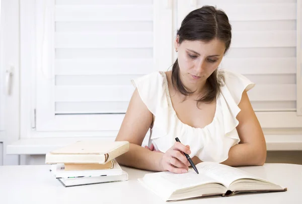Dívka s učebnice připraví na zkoušky na univerzitě. Mladá brunetka učí ponaučení. Žena na zasedání. Student na ubytovně čte knihy. Stock Obrázky