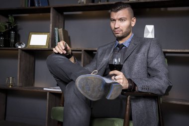 Çekici genç yakışıklı şık erkek takım elbise kırmızı şarap ile sandalyede oturur. Şık zarif adam lüks iç daire.