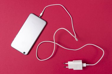 modern smartphone ve pembe bir arka plan üzerinde bağlı şarj kablosu.
