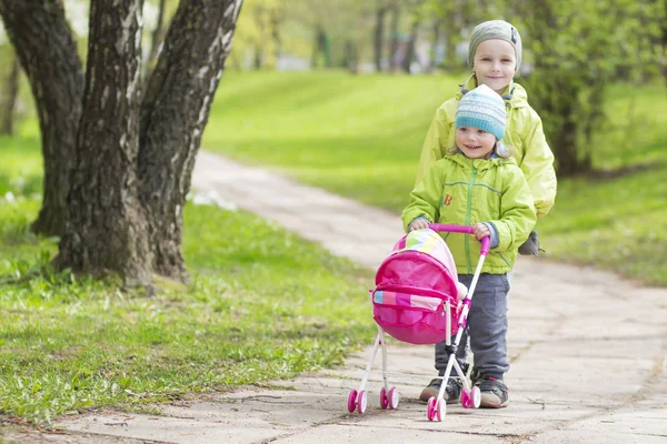 Adik dan adik kecil mengendarai kereta bayi mainan di taman. — Stok Foto