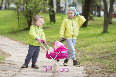 Two children baby girl and boy playing in the yard with a toy stroller. clipart