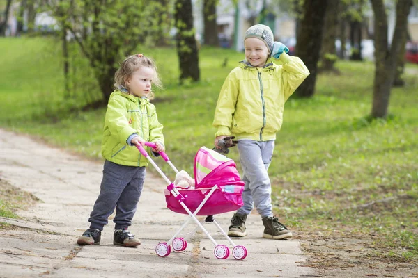 Dua anak perempuan dan anak laki-laki bermain di halaman dengan kereta bayi mainan . — Stok Foto