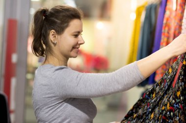 Genç bir kadın, bir moda giyim butik bir elbise seçer. Mağazada alışveriş.