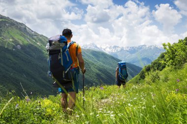 Sırt çantaları dağ hiking ile turistler Svaneti içinde yaz gününde yürüyüş. Genç çocuklar Georgia Dağları aşarak patika boyunca gidin. Turist güzel dağ manzarası