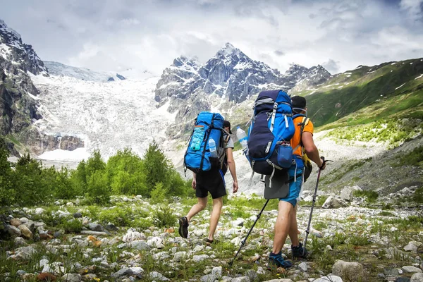 İki yürüyüşçü dağlarında büyük sırt çantaları ile. Turistler üzerinde Kayalık Dağları zammı. Dağ Trek boş zaman etkinliği. Macera vahşi Svaneti bölgesi Gürcistan'ın adamlarından. Groupe Hiking. — Stok fotoğraf