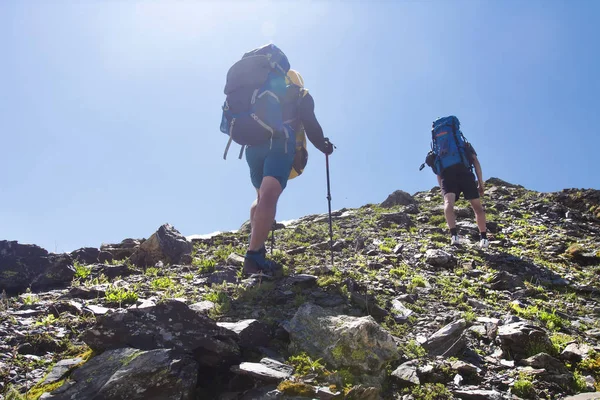 Vista em dois escaladores monte de caminhada para o pico da montanha. Atividades de lazer nas montanhas. Caminhadas desportivas em Svaneti, Geórgia. Escalada. Turistas com mochilas na encosta rochosa. Caminhantes em caminhada de montanha . — Fotografia de Stock