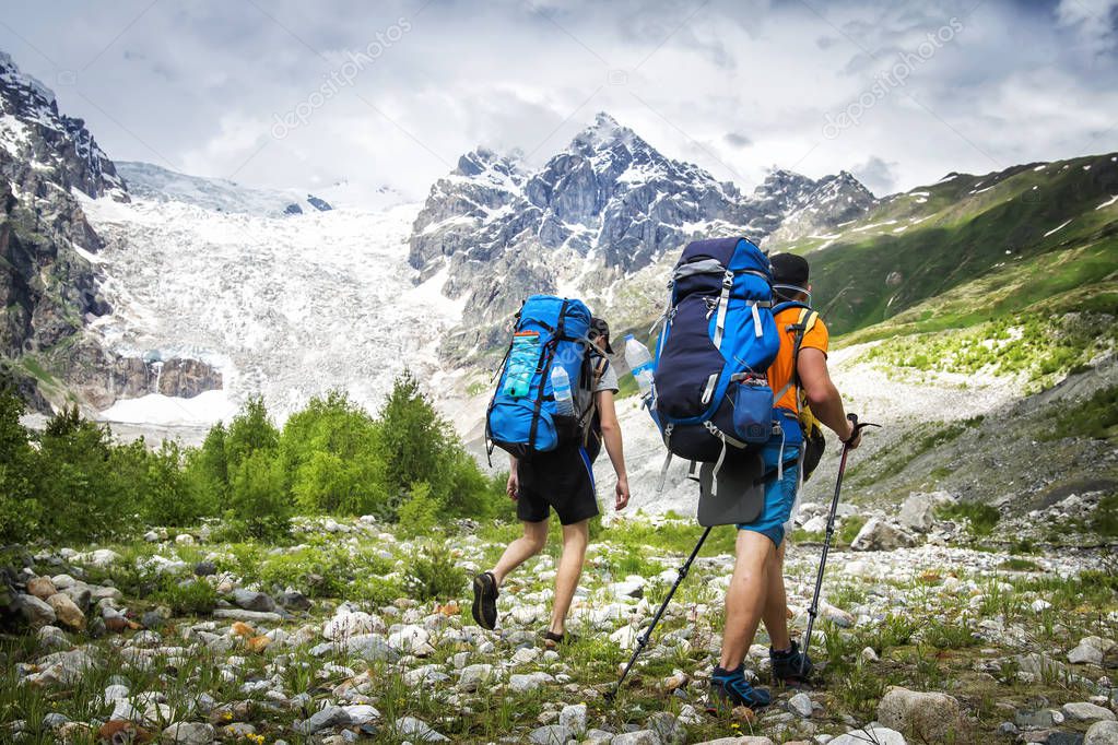 Two hikers with large backpacks in mountains. Tourists hike on rocky mounts. Leisure activity on mountain trek. Adventure of men in wild Svaneti region of Georgia. Groupe Hiking.