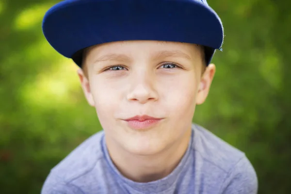Portrait of beautiful little white boy in cap in green summer park on sunny day. — Stok Foto