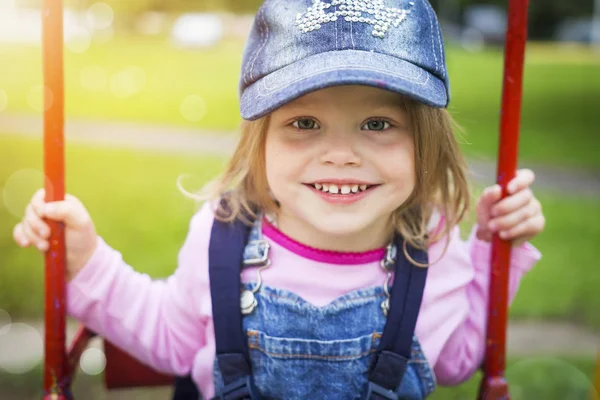 Портрет красивой улыбающейся маленькой девочки в летнем парке на качелях. Счастливый милый ребенок катается на качелях — стоковое фото