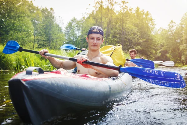 Rowers in a kayak with oars sail along the river on a bright summer day. Young athletic men row oars on the water in boat. Leisure. Healthy lifestyle. Adventures of group of young people in nature