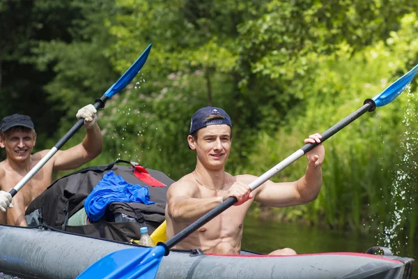 Junge sportliche Männer in Ruderbooten rudern an einem Sommertag entlang des Flusses. Kanu. Freunde schwimmen im Kajak. Aktive Erholung in der Natur. Gesunder Lebensstil — Stockfoto