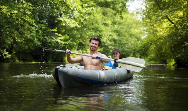 Молодые парни в лодке с веслами на реке на фоне зеленых деревьев над водой. Каякеры на каяке с веслами в руках улыбаются. Два человека в каноэ. Рафтинг на реке на каяке. Досуг . — стоковое фото