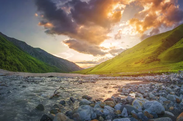 Atemberaubende Berglandschaft bei Sonnenuntergang. Steine im Vordergrund und Hochland vor buntem Himmel mit Wolken. malerischer Blick auf den Berg im warmen Sonnenlicht vom Fluss. svaneti nature georgia. schöne Hügel. — Stockfoto