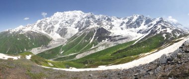 Svaneti mountains landscape in Georgia. Caucasian ridge with snowy mountain peaks and green grass on bright sunny summer day. High mountains in Svaneti. Natural panoramic view on mounts in Georgia clipart