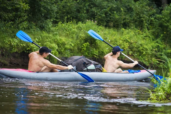 Два молодых спортсмена в лодке гребли на веслах по воде. Катание на байдарках по реке в летний сезон. Рафтинг на реке в каноэ — стоковое фото
