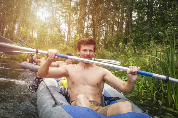 Ein junger, sportlicher Mann im Kajak mit Ruder. Kanufahren auf dem Fluss während der Sommersaison. Aktive Erholung in der Natur. Freunde schwimmen in einem Boot auf dem Fluss — Stockfoto